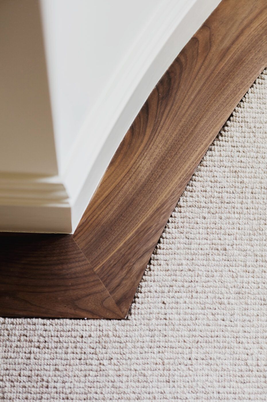 Curved walnut skirting meeting a white column base and wool carpet